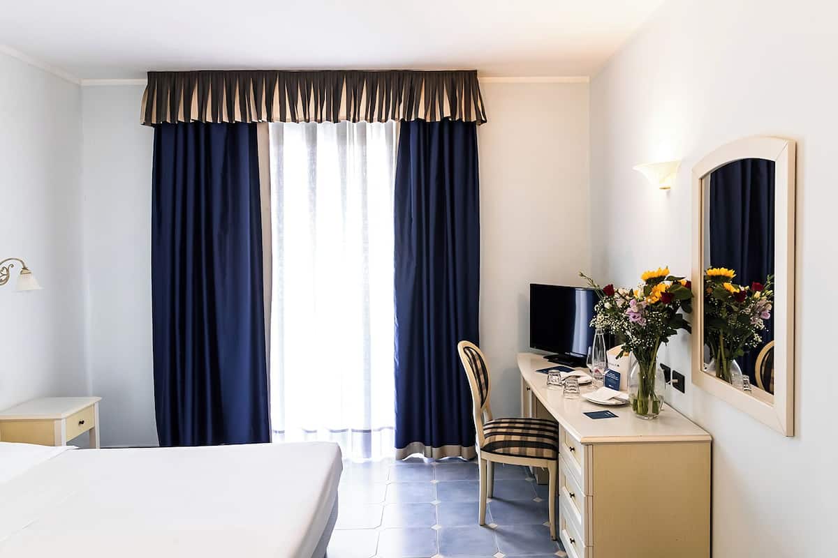 Une chambre d’hôtel comprenant un lit, un bureau avec un ordinateur, une chaise, une télévision et un miroir.