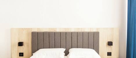 Una cama con cabecera de madera y dos mesitas de noche, cada una con un objeto cuadrado negro al lado.