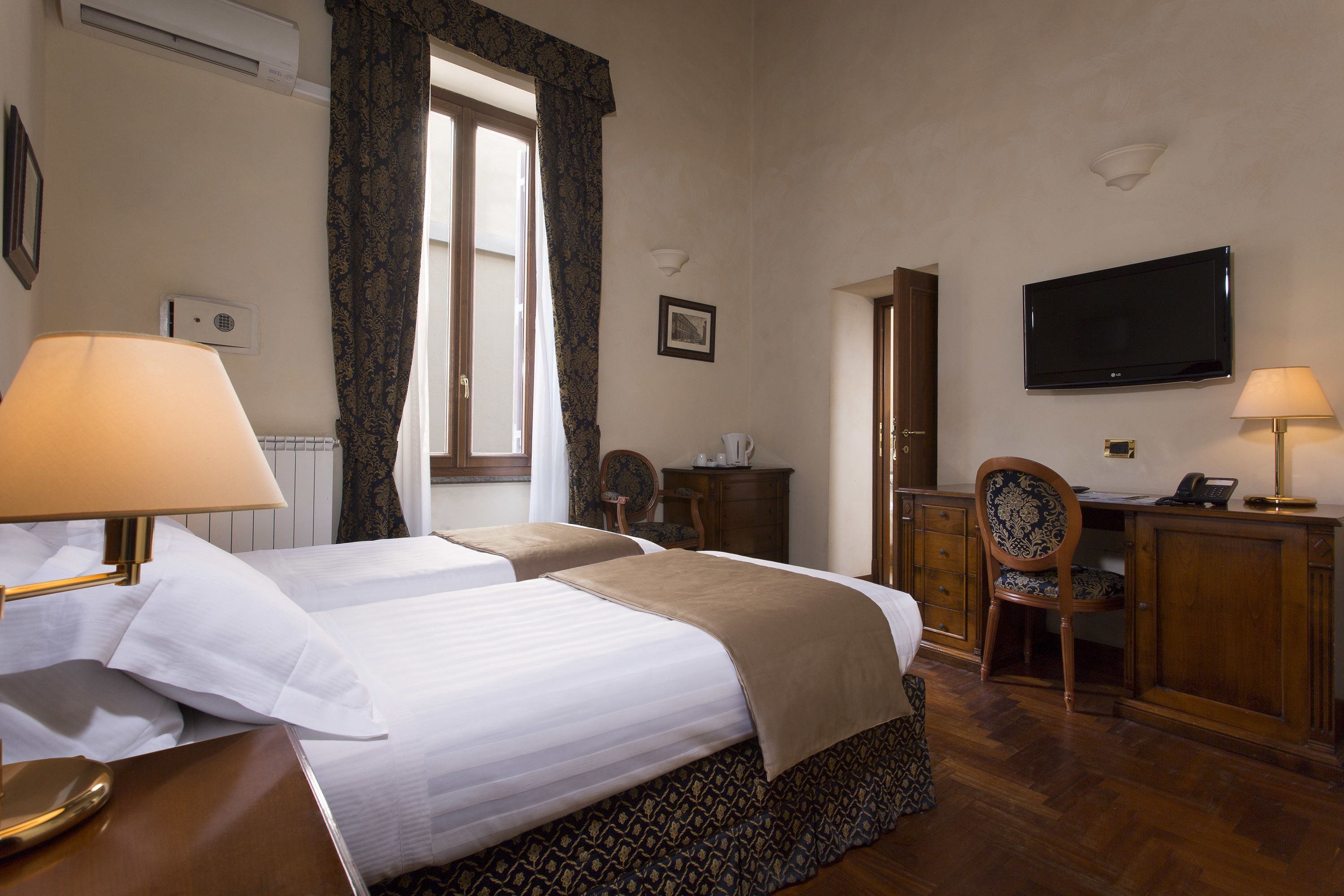 A hotel room with two beds, a desk, a chair, a television, and a window with curtains.