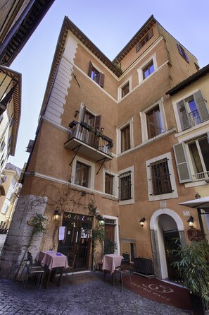 A courtyard with tables and chairs, a door with a sign, and a building with multiple windows and balconies. - Hotel Teatro Pace (Rome)