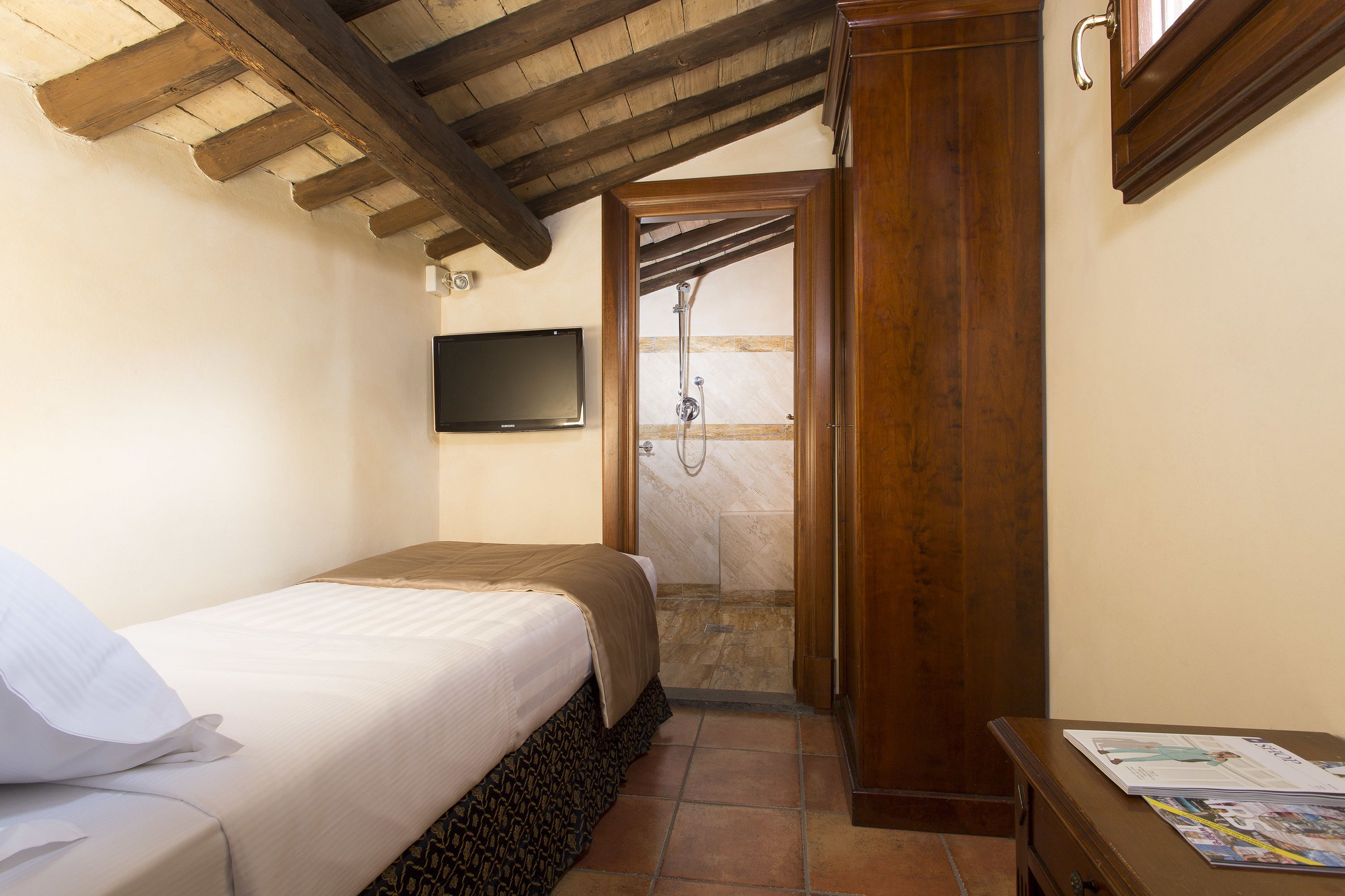 A bedroom with a bed, a wooden door, a shower area, and a flat-screen TV on the wall.