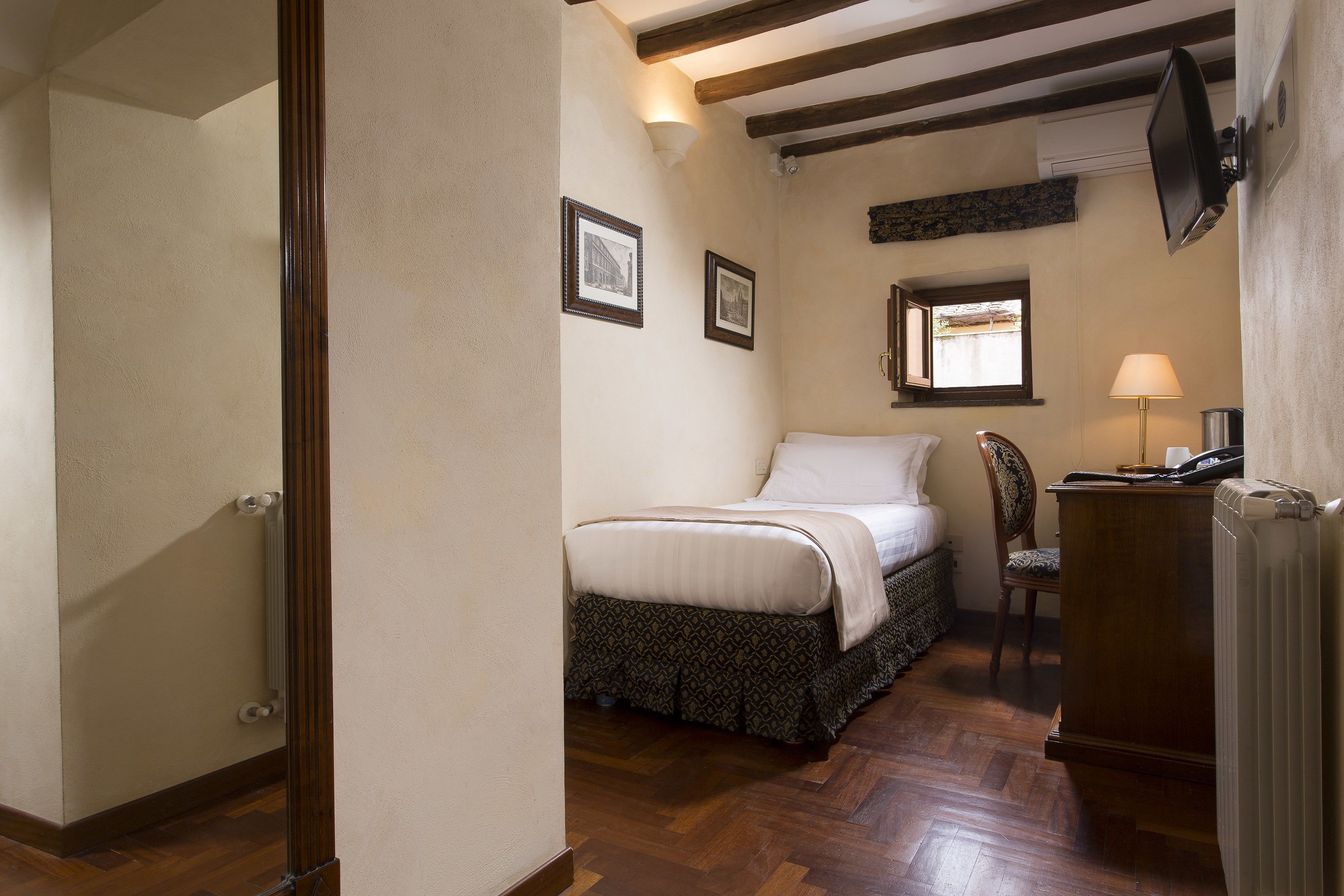 Une chambre à coucher comprenant un lit, une chaise, un bureau, une lampe et un téléviseur fixé au mur.