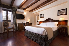 A hotel room with a large bed, wooden floor, a television, a desk, and two lamps. - Hotel Teatro Pace (Rome)
