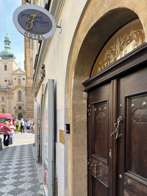 Un cartello di un albergo, una porta in legno e una facciata con elementi architettonici.