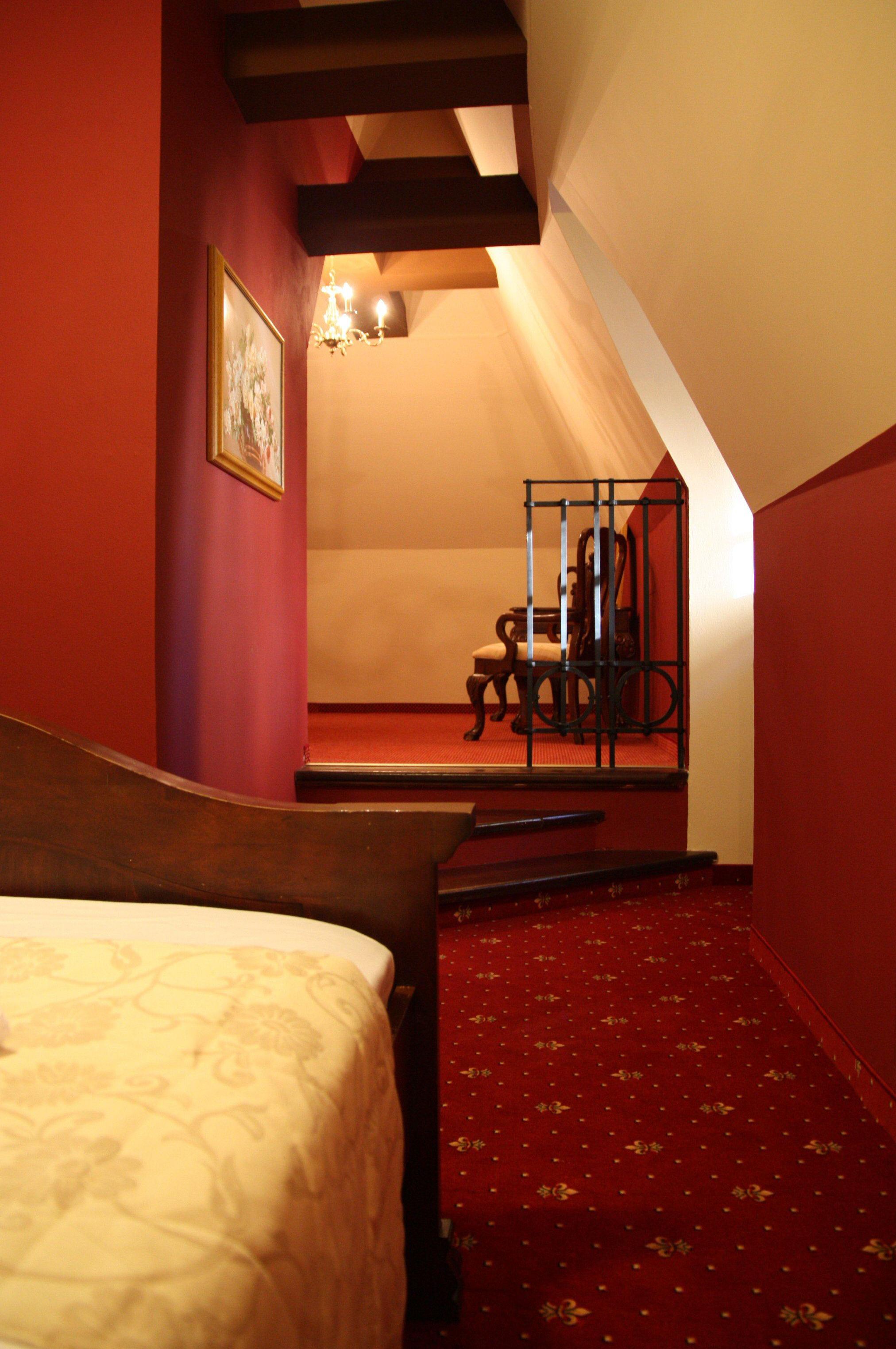 A bedroom with a wooden bed, a red carpet, a chandelier, and a chair in the corner.