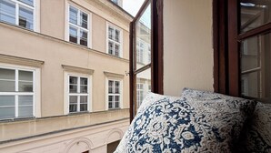 Una habitación con un ventanal amplio, un cojín estampado y vistas a un edificio con múltiples ventanas.