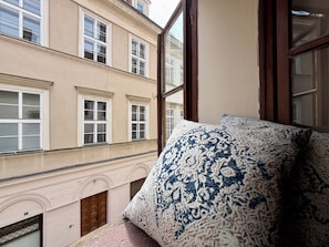A room with a large window, a patterned pillow, and a view of a building with multiple windows. - Prague Golden Age (Prague)