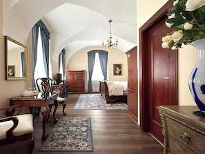 A bedroom with a bed, a dresser, a desk, and a chair. There is a chandelier and a vase with flowers. - Prague Golden Age (Prague)