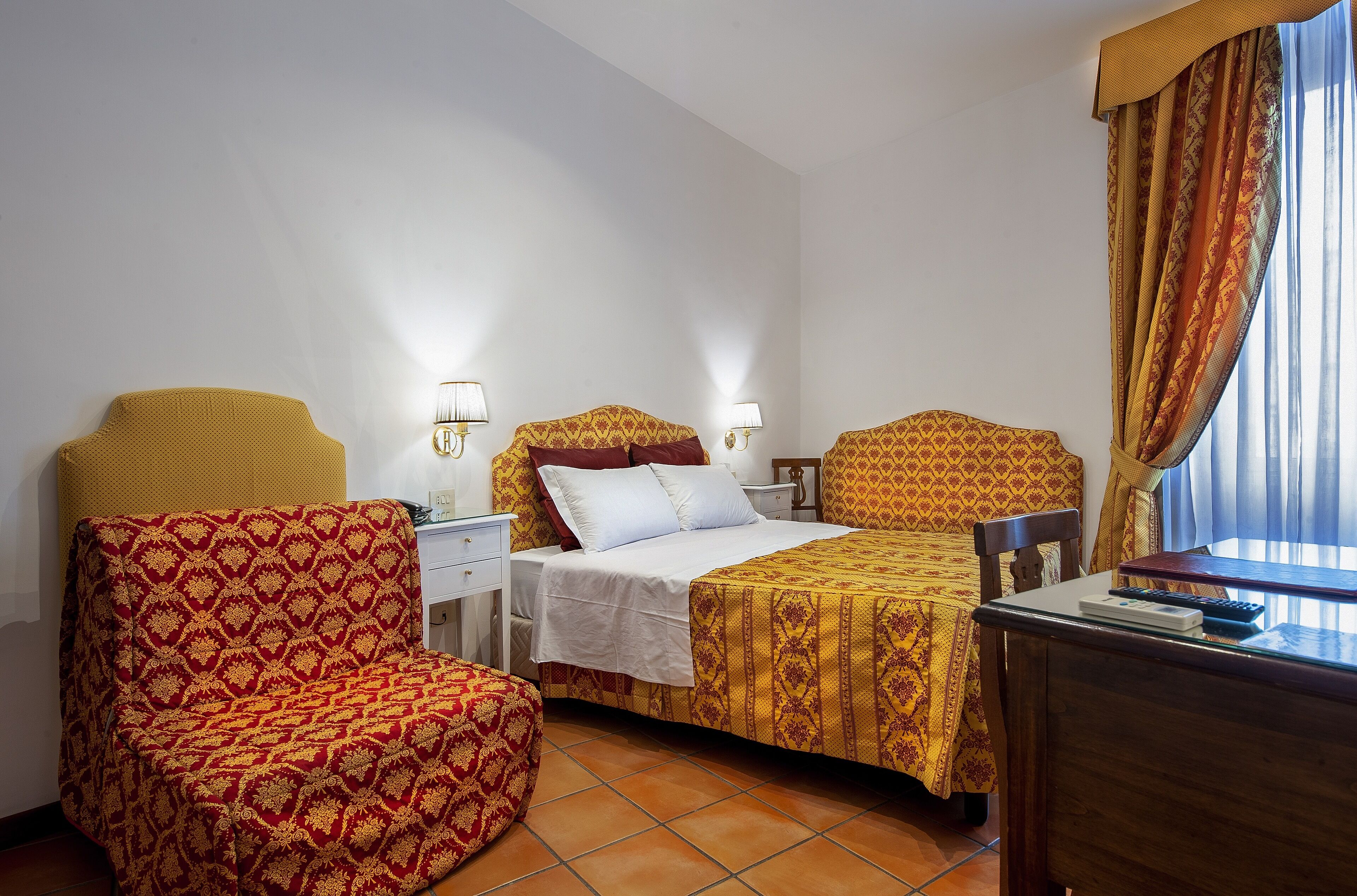 Ein Hotelzimmer mit Bett, Sessel, Schreibtisch und einem Fenster mit Vorhängen.
