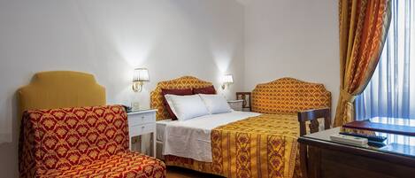 A hotel room with a bed, a chair, a desk, and a window with curtains.
