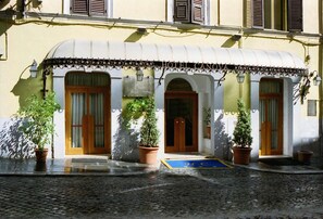 A hotel facade with a curved roof, wooden doors, and potted plants. - Hotel Canova (Rome)