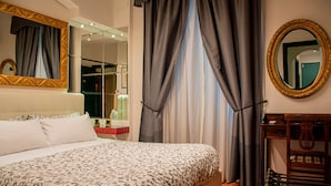 Une chambre d’hôtel avec un grand lit, un miroir doté d’un cadre orné, une table de chevet en bois et une fenêtre avec des rideaux.