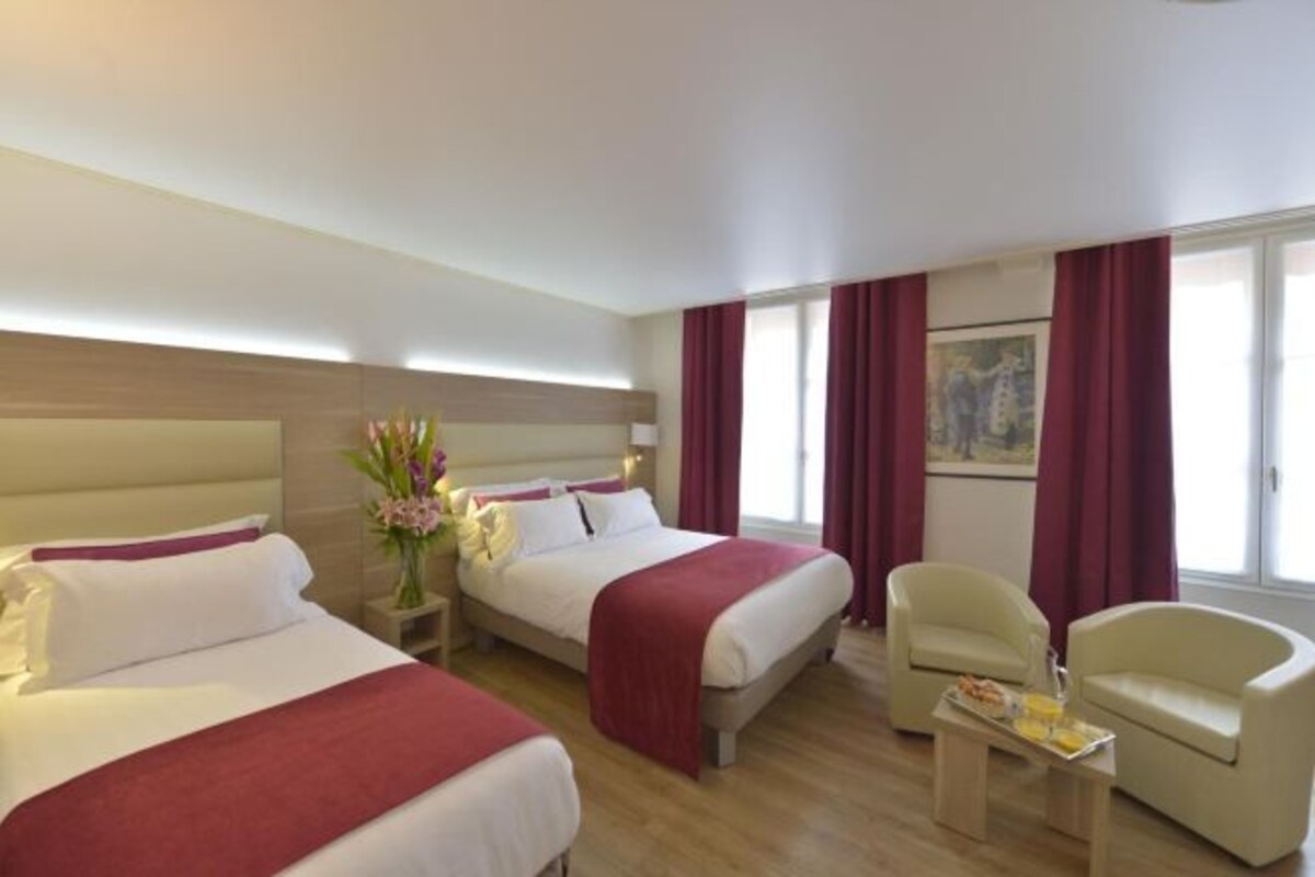 Une chambre d’hôtel avec deux lits, un coin salon comprenant un fauteuil, une petite table et un tableau au mur.