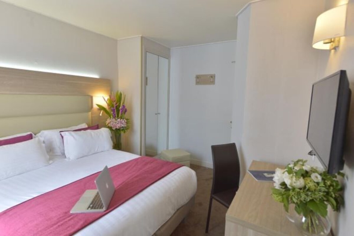 Une chambre d’hôtel avec un lit, un bureau avec un ordinateur portable, une chaise, une télévision et un vase avec des fleurs.