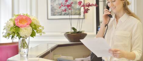 A reception desk with a vase of flowers, a framed picture on the wall, and a person holding a paper.