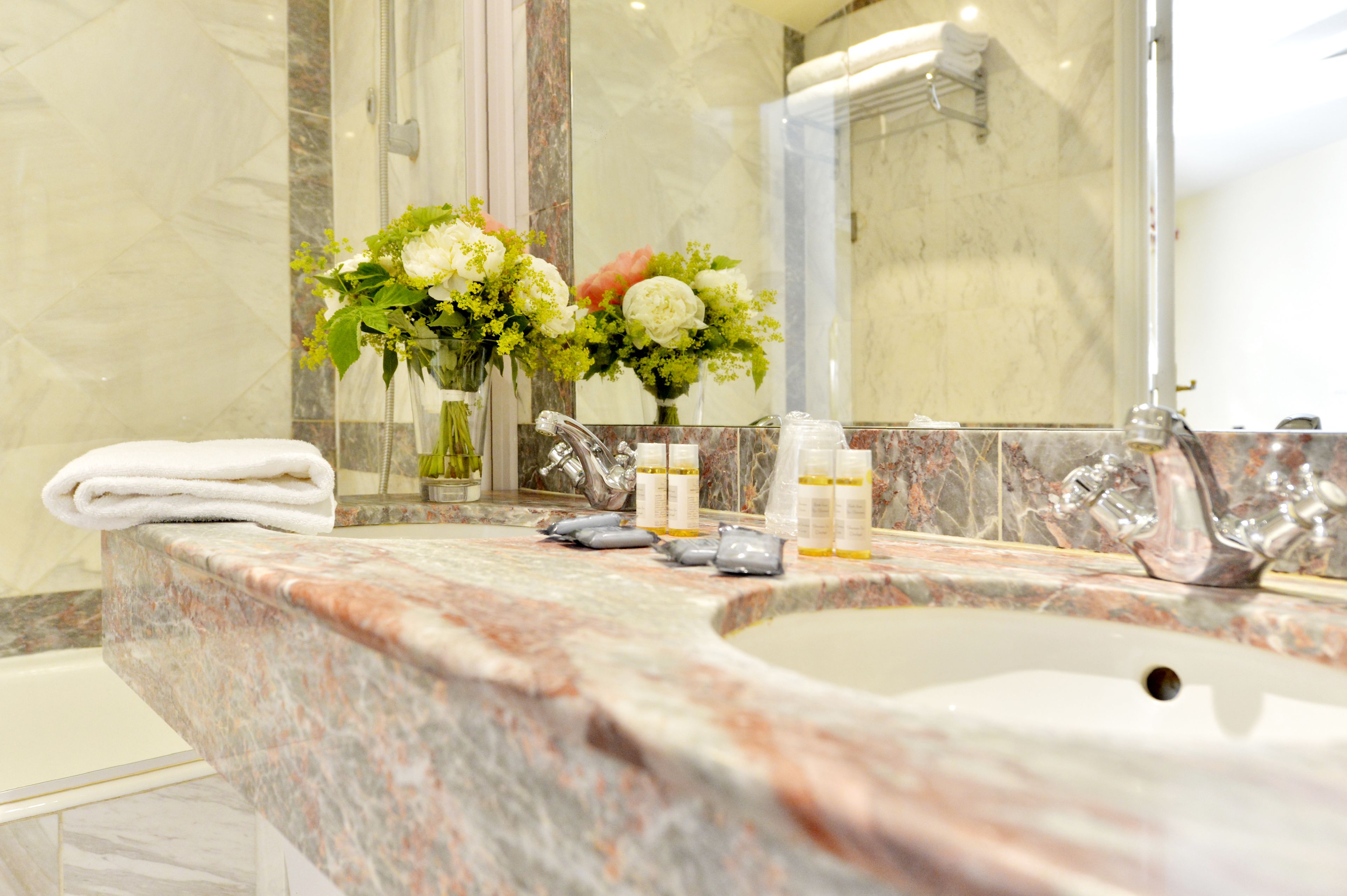 Un baño con lavamanos de mármol, dos llaves y un florero.