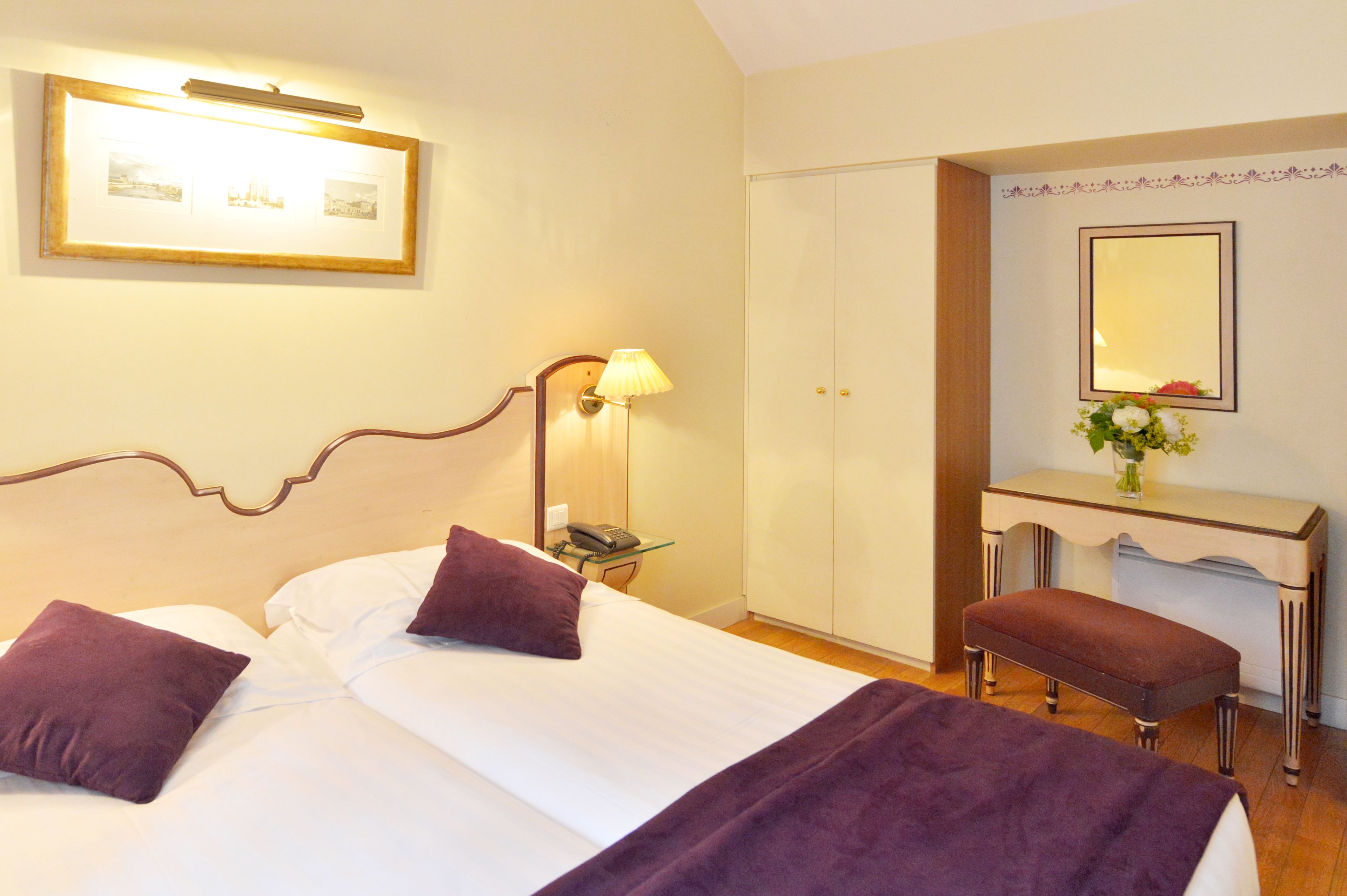 A hotel room with a bed, bedside table, lamp, wardrobe, bench, and a mirror.