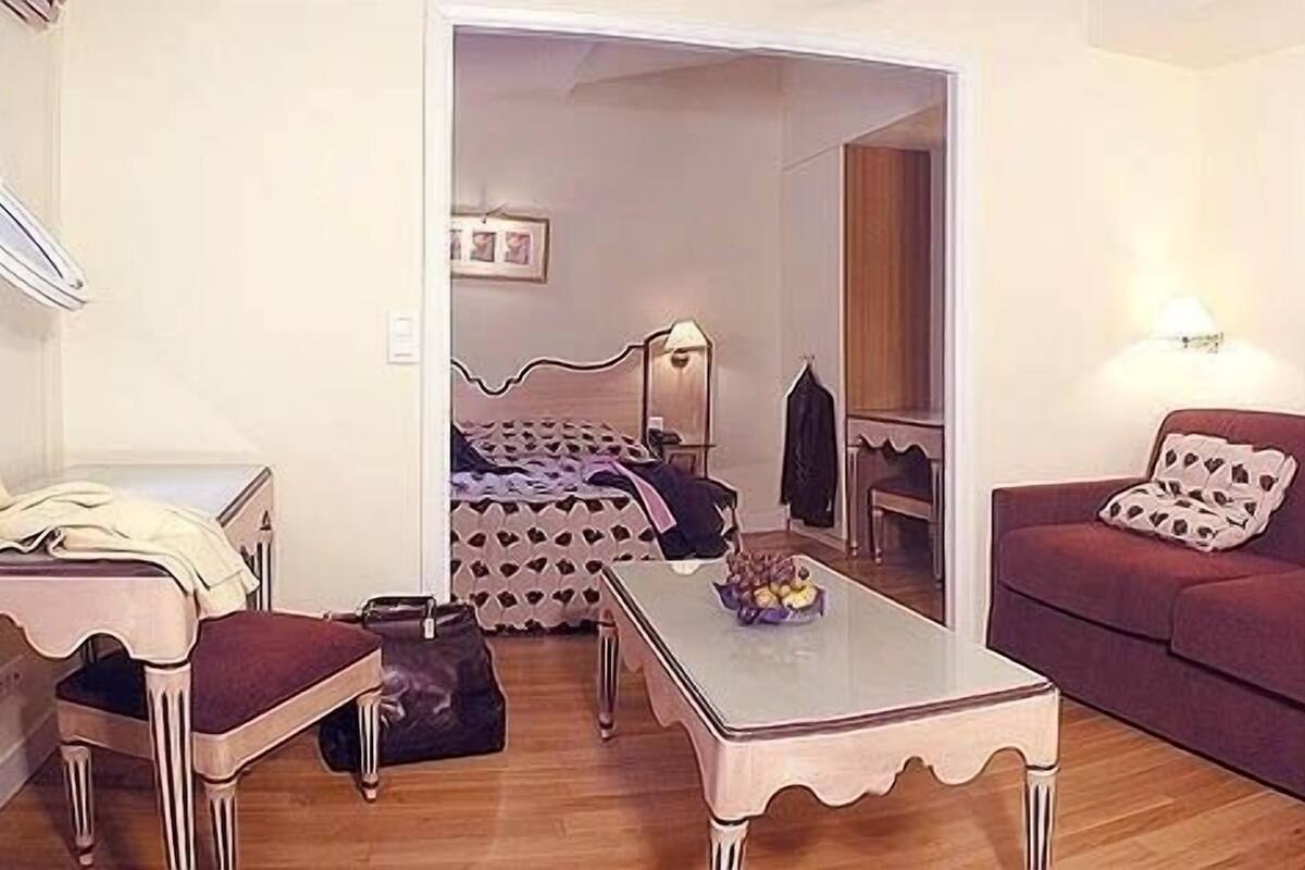Ein Zimmer mit einem Bett, einem Schlafsofa, einem Tisch und einem Stuhl. Eine Tür führt in einen weiteren Raum.