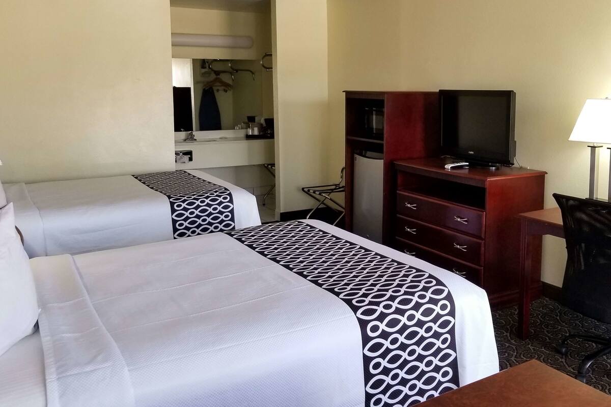 A hotel room with two beds, a desk, a chair, a television, and a mirror.