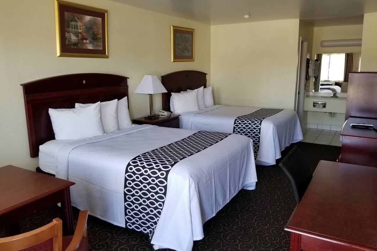 A hotel room with two beds, a desk, a chair, and a dresser.