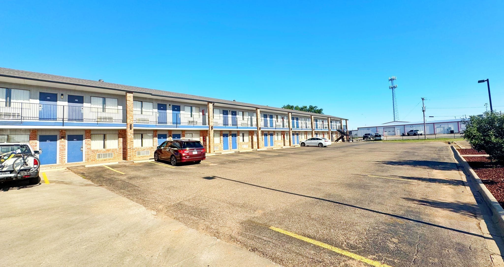 Un motel avec plusieurs chambres, un parking et un bâtiment en arrière-plan.