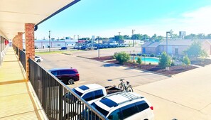 A parking lot with several cars, a building with a brick facade, and a swimming pool area.