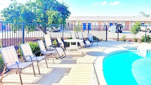 Zona junto a la piscina con sillas reclinables y una pequeña mesa, rodeada por una valla.