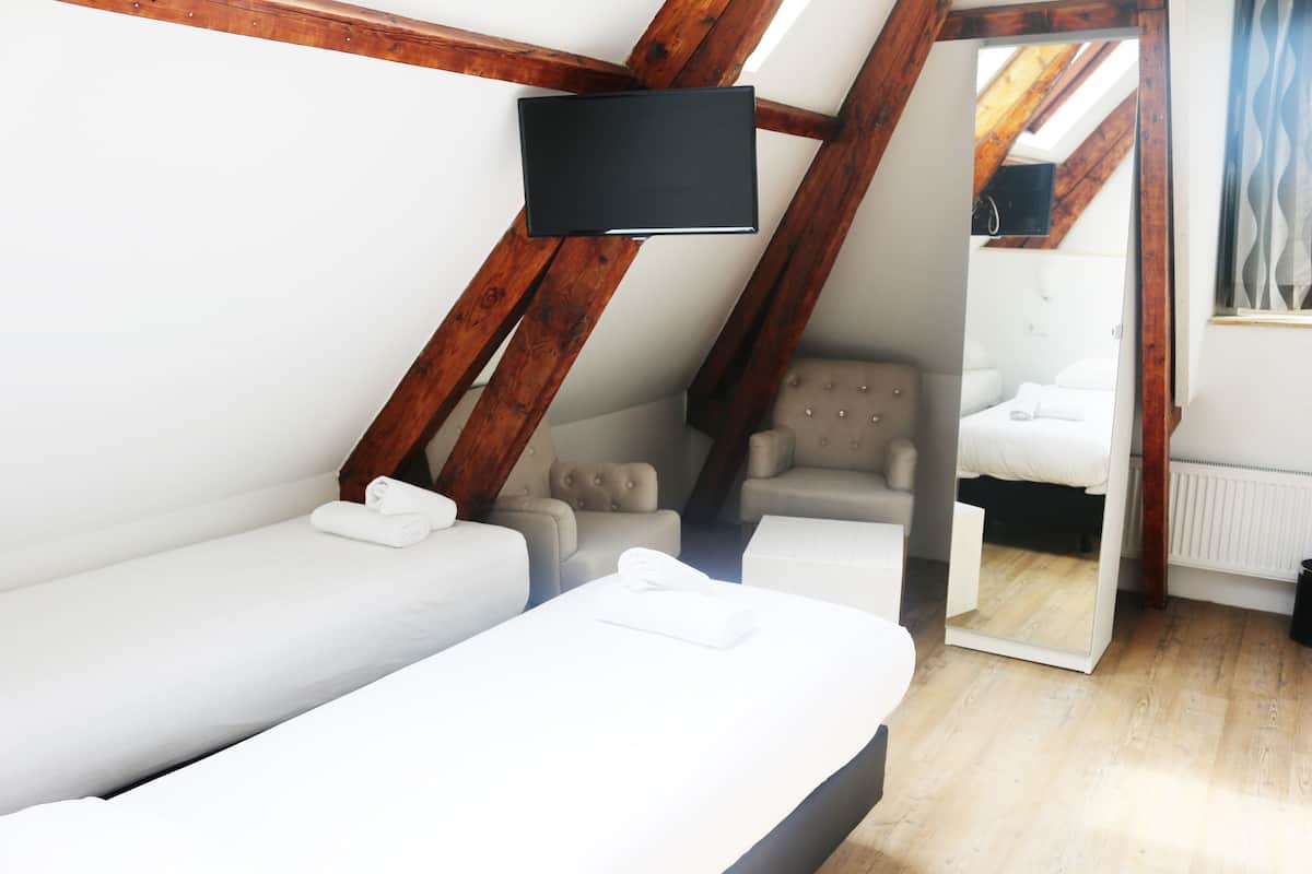 A room with a sloped ceiling, a bed, a sofa, a chair, and a television.
