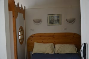 A bedroom with a wooden headboard, a bed with two pillows, a framed picture on the wall, and a circular mirror on the left. - Hôtel Montpellier (Paris)