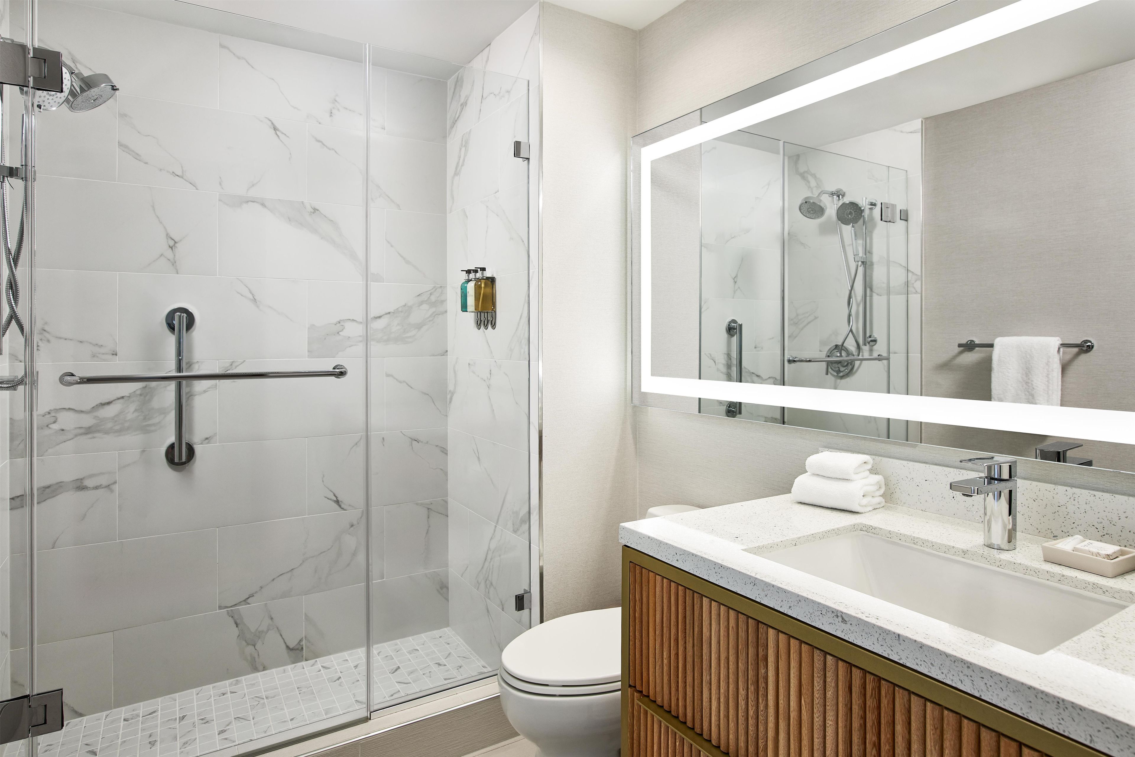 A modern bathroom with a glass-enclosed shower, a vanity with a marble countertop, and a large mirror above the sink.