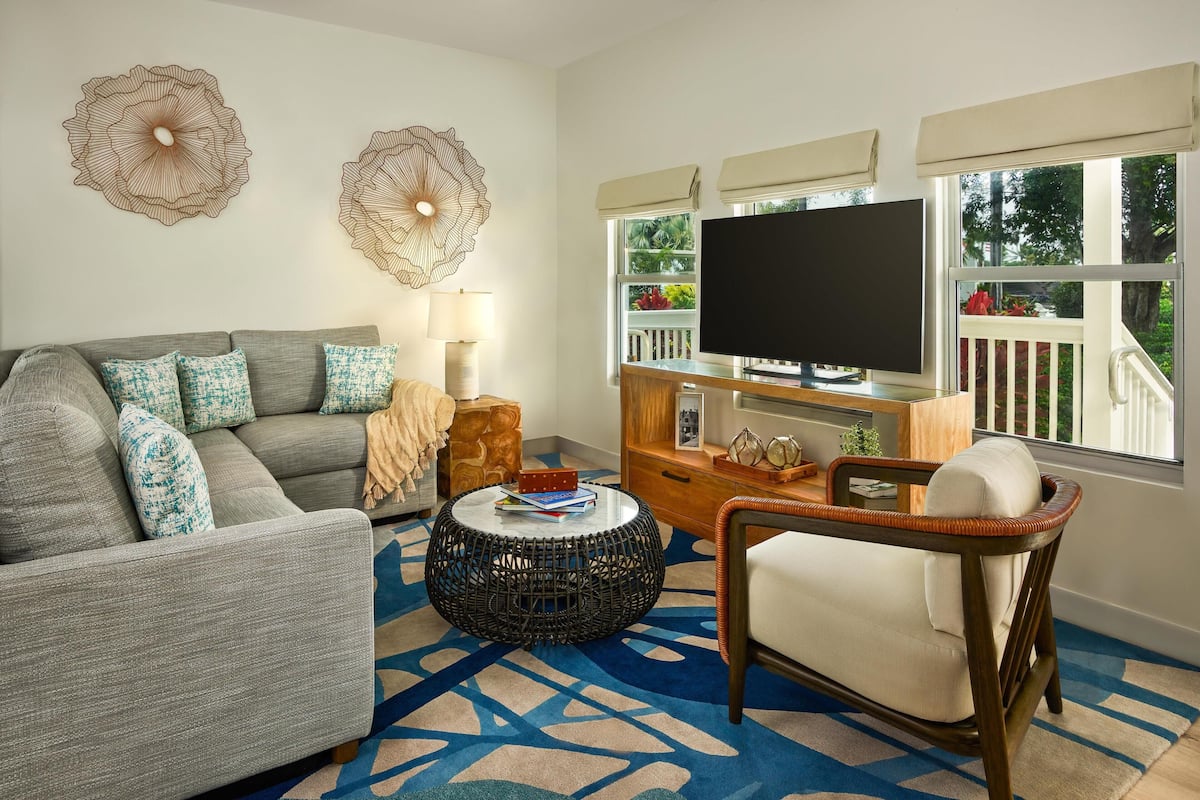 A living room with a grey sofa, a wicker coffee table, a wicker armchair, a flat-screen TV, and decorative wall art.