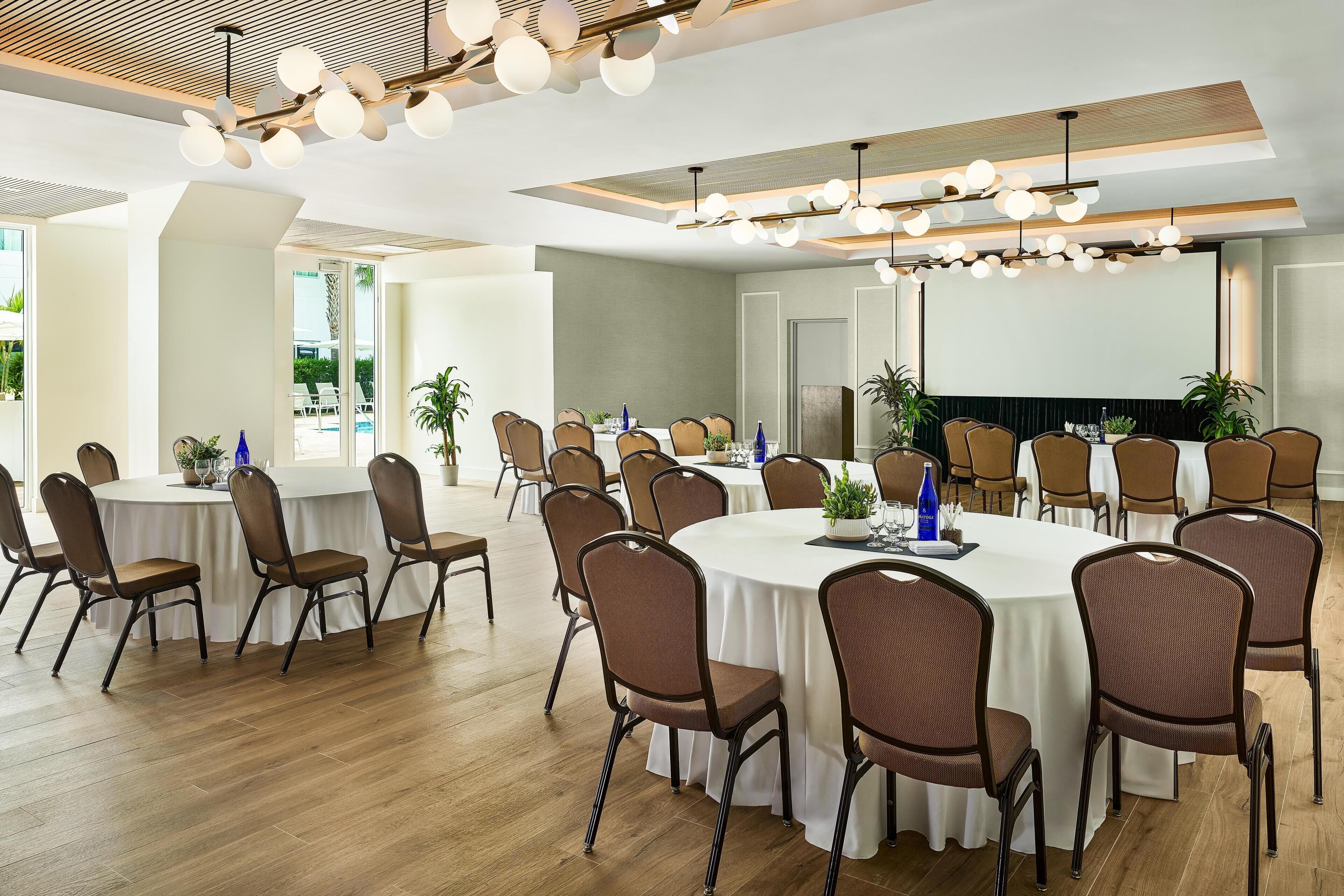 A conference room with round tables, chairs, and a large screen.
