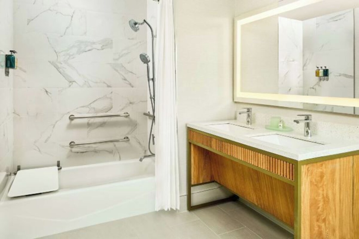 Un baño moderno con pared de mármol, tocador de madera, un espejo grande y zona de ducha.