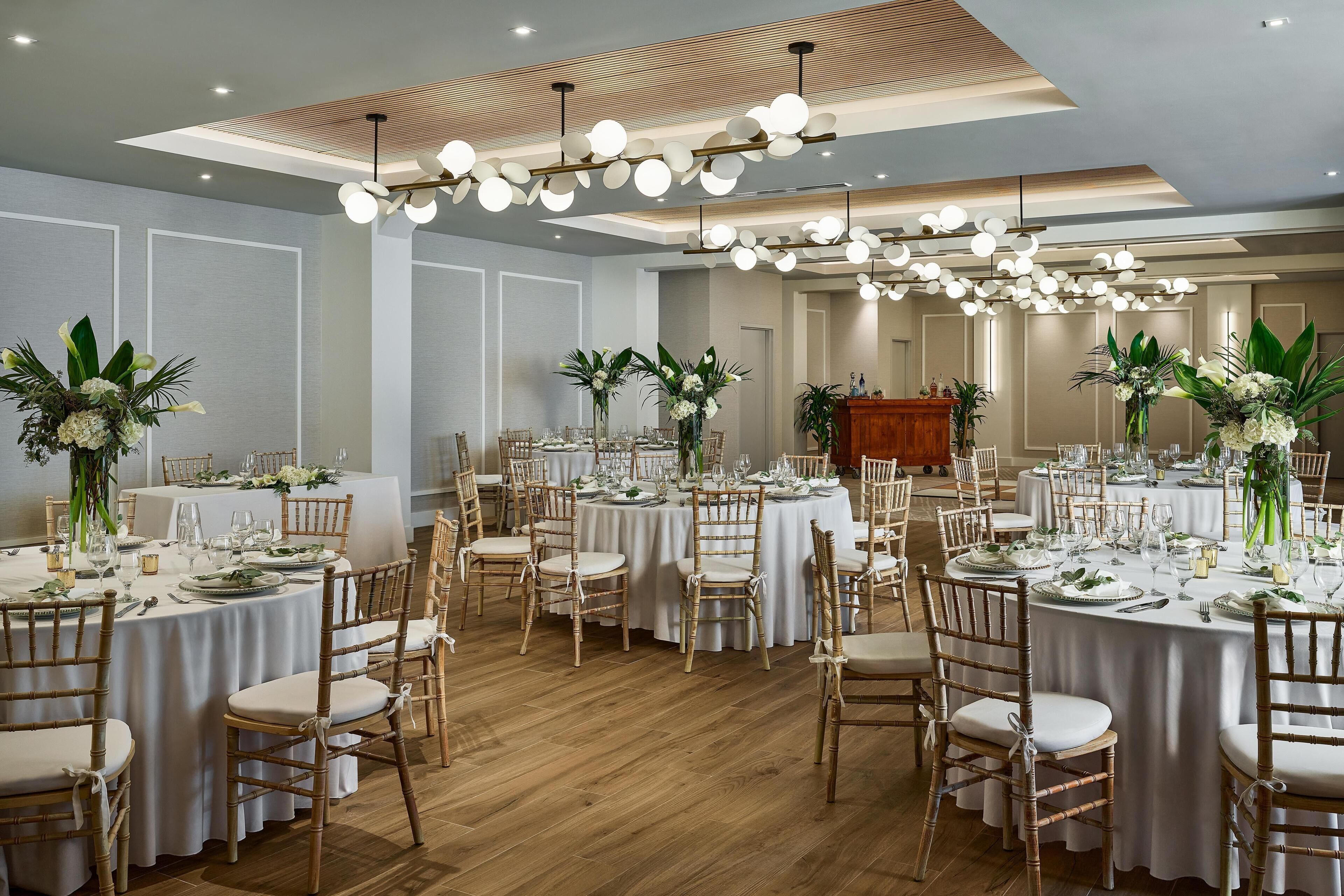 A spacious banquet hall with round tables, white tablecloths, and wooden chairs.