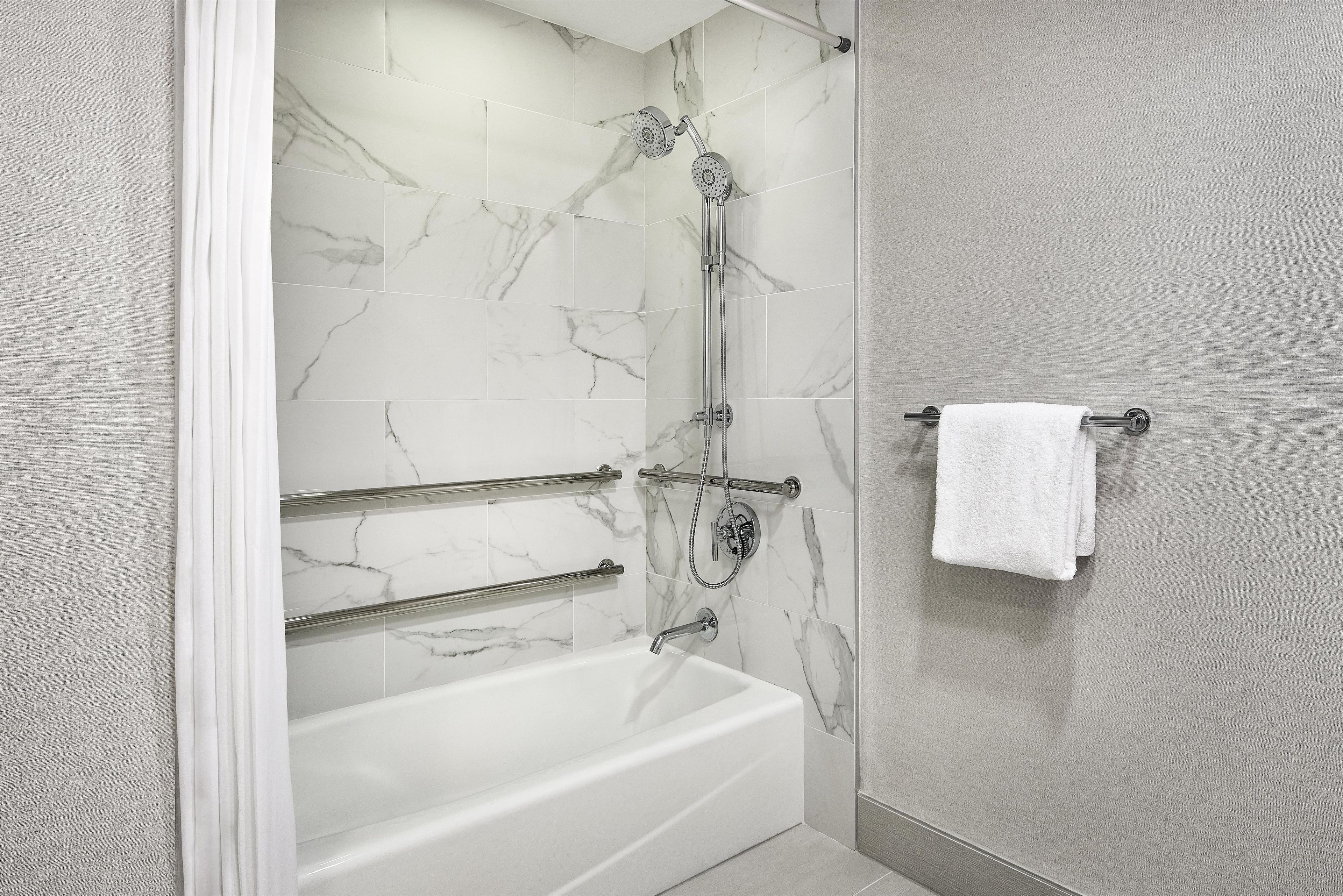 Ein Badezimmer mit einer Badewanne, einer Dusche inklusive Duschbrause und einem Handtuchhalter mit einem weißen Handtuch.