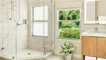 A modern bathroom with a glass-enclosed shower, a wooden vanity, a large mirror, and a window with a view of greenery.