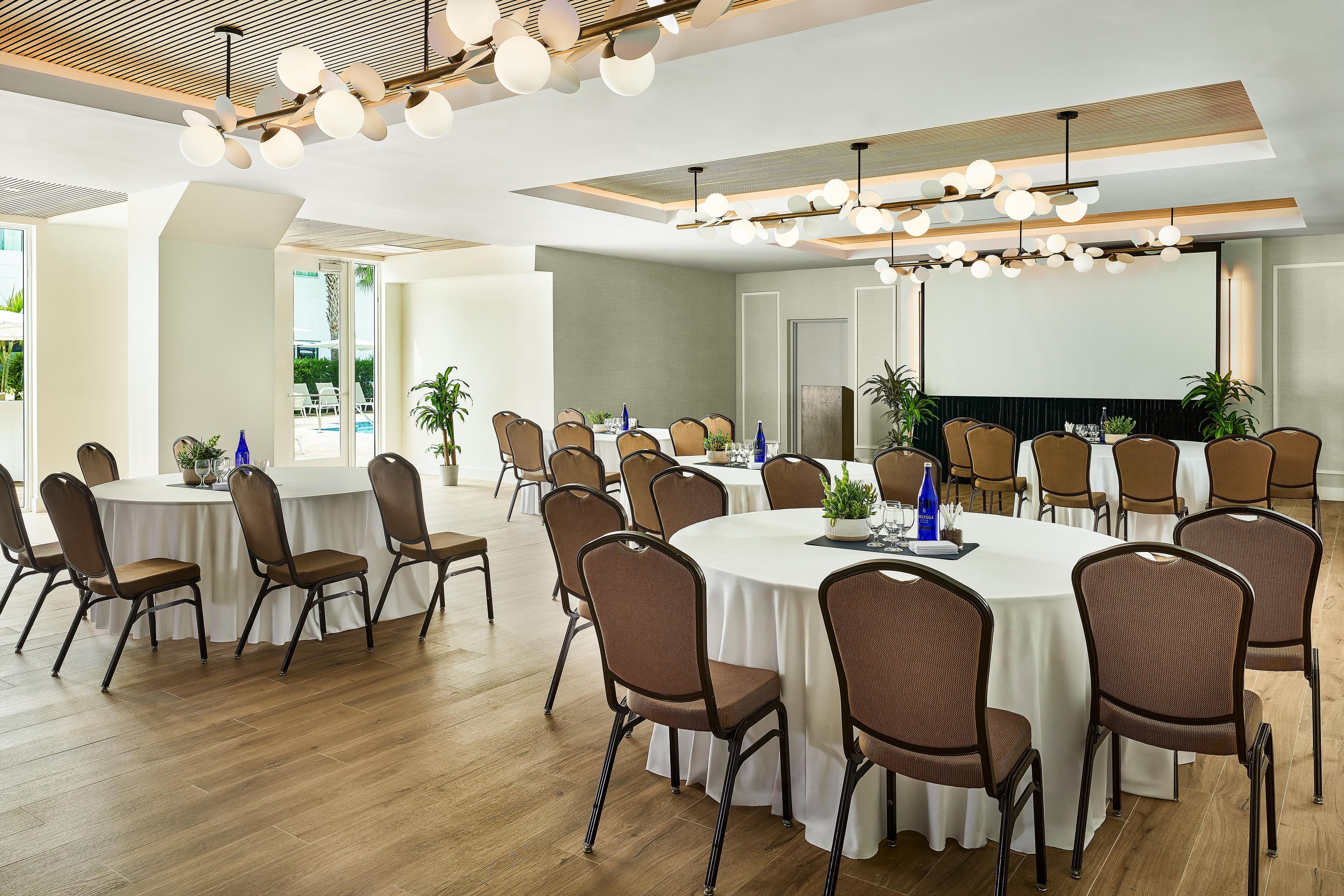 A conference room with round tables, chairs, and a large screen.
