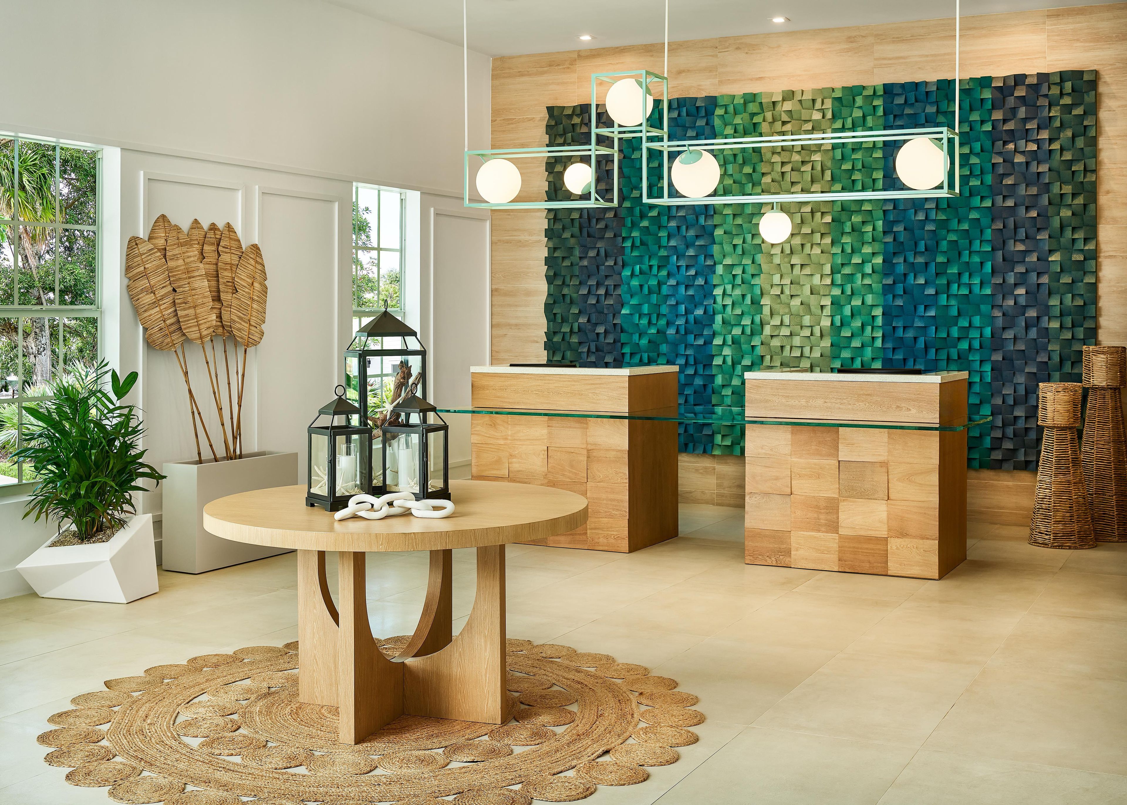 A modern interior with a round wooden table, two glass-top side tables, and a textured wall.