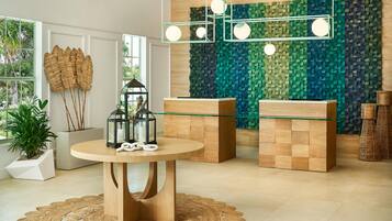 A modern interior with a round wooden table, two glass-top side tables, and a textured wall.