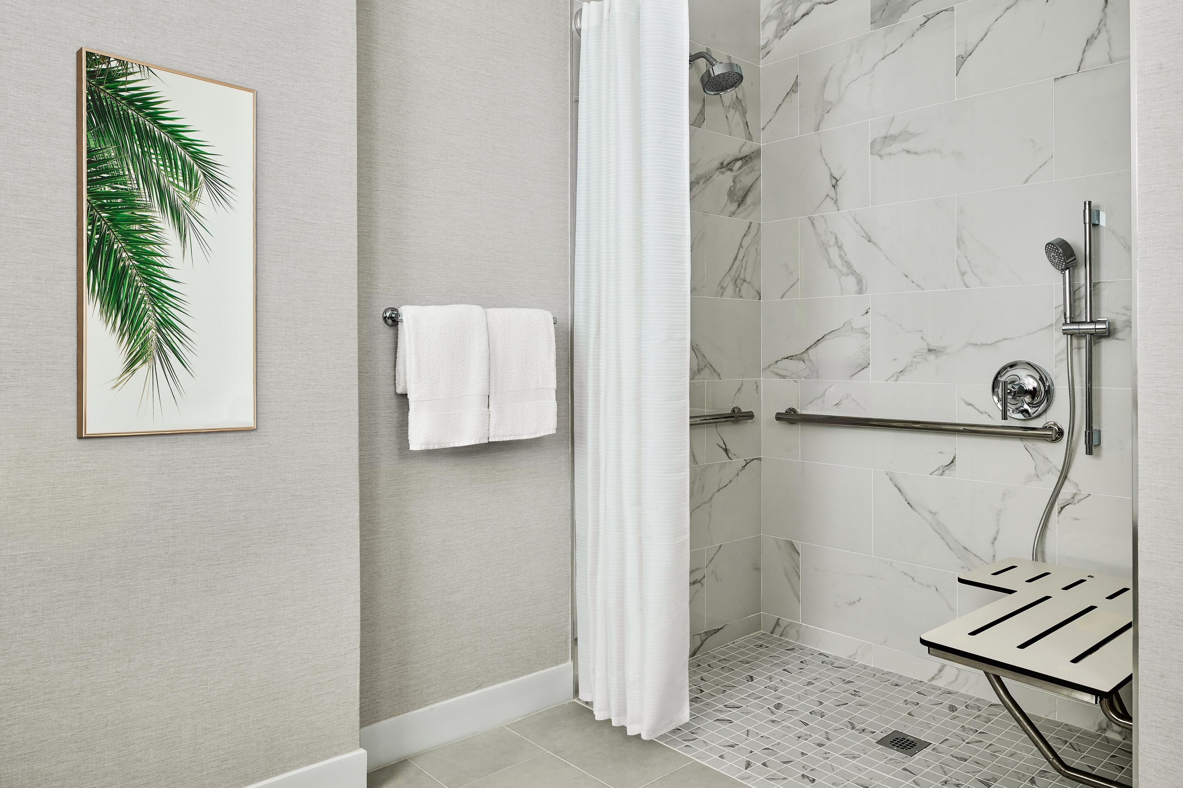 A modern bathroom with a shower, marble tiles, a towel rack, and a framed plant.