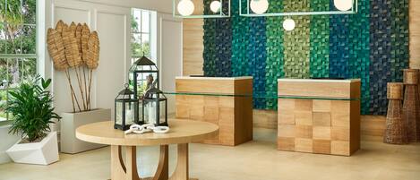 Un intérieur moderne avec une table ronde en bois, un comptoir d’accueil avec un plateau en verre et un mur orné d’un motif texturé.