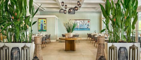 A spacious lobby with a central round table, surrounded by wicker chairs, large potted plants, and decorative lanterns.
