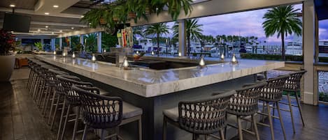 A bar area with a long counter, multiple stools, and a view of the marina with boats.