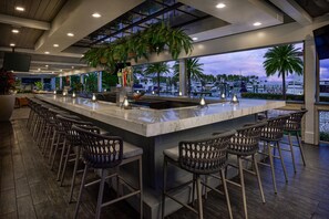 A bar area with a long counter, multiple stools, and a view of the marina with boats. - Faro Blanco Resort Marathon Florida Keys, Curio by Hilton (Marathon)