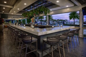 Zona de bar con una barra larga, varios taburetes y vistas al puerto deportivo con barcos.