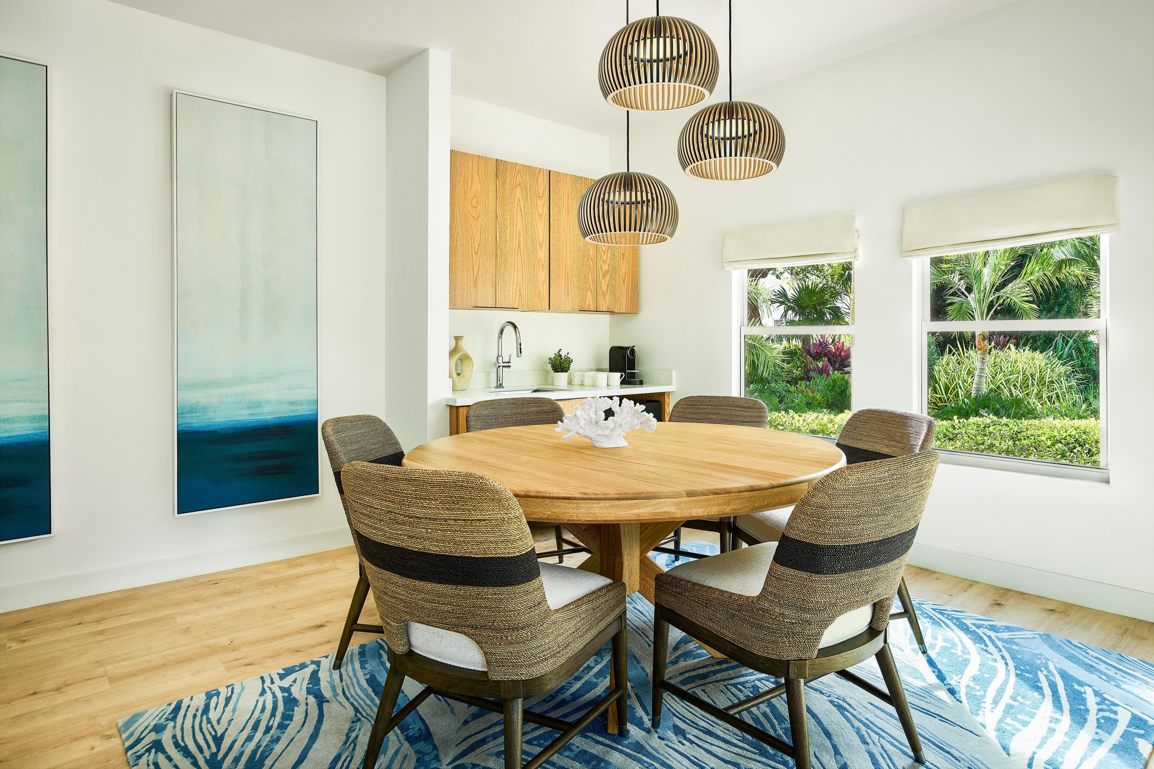 A dining area with a round wooden table, wicker chairs, and a blue patterned rug.