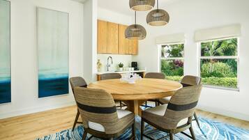 A dining area with a round wooden table, wicker chairs, and a blue patterned rug.