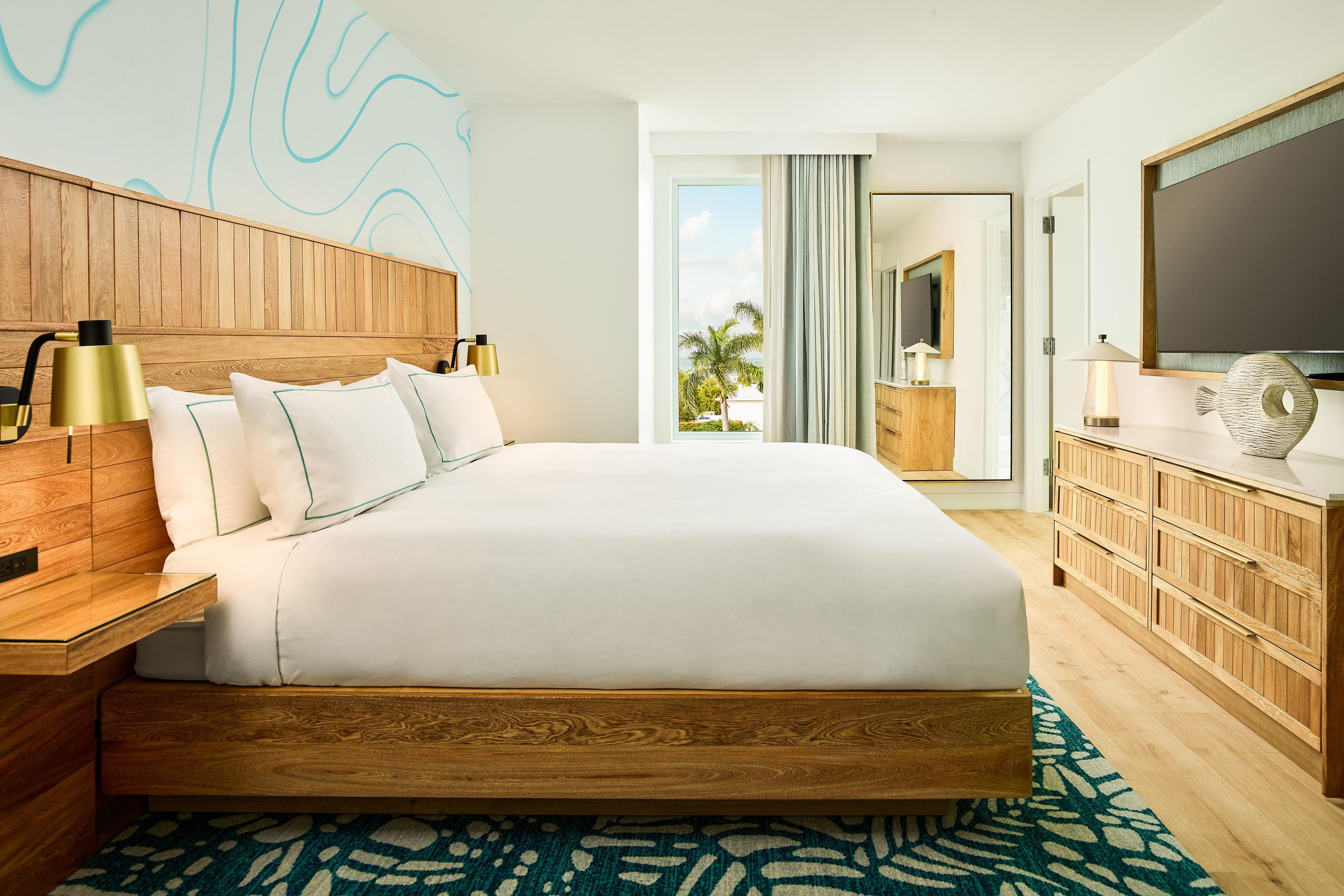 Habitación de hotel moderna con una cama grande, cabecera de madera, mesitas de noche, cómoda y televisor.