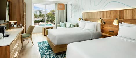 Ein Hotelzimmer mit zwei Betten, einem Schreibtisch, einem Sessel, Blick auf den Pool und einem Essbereich.