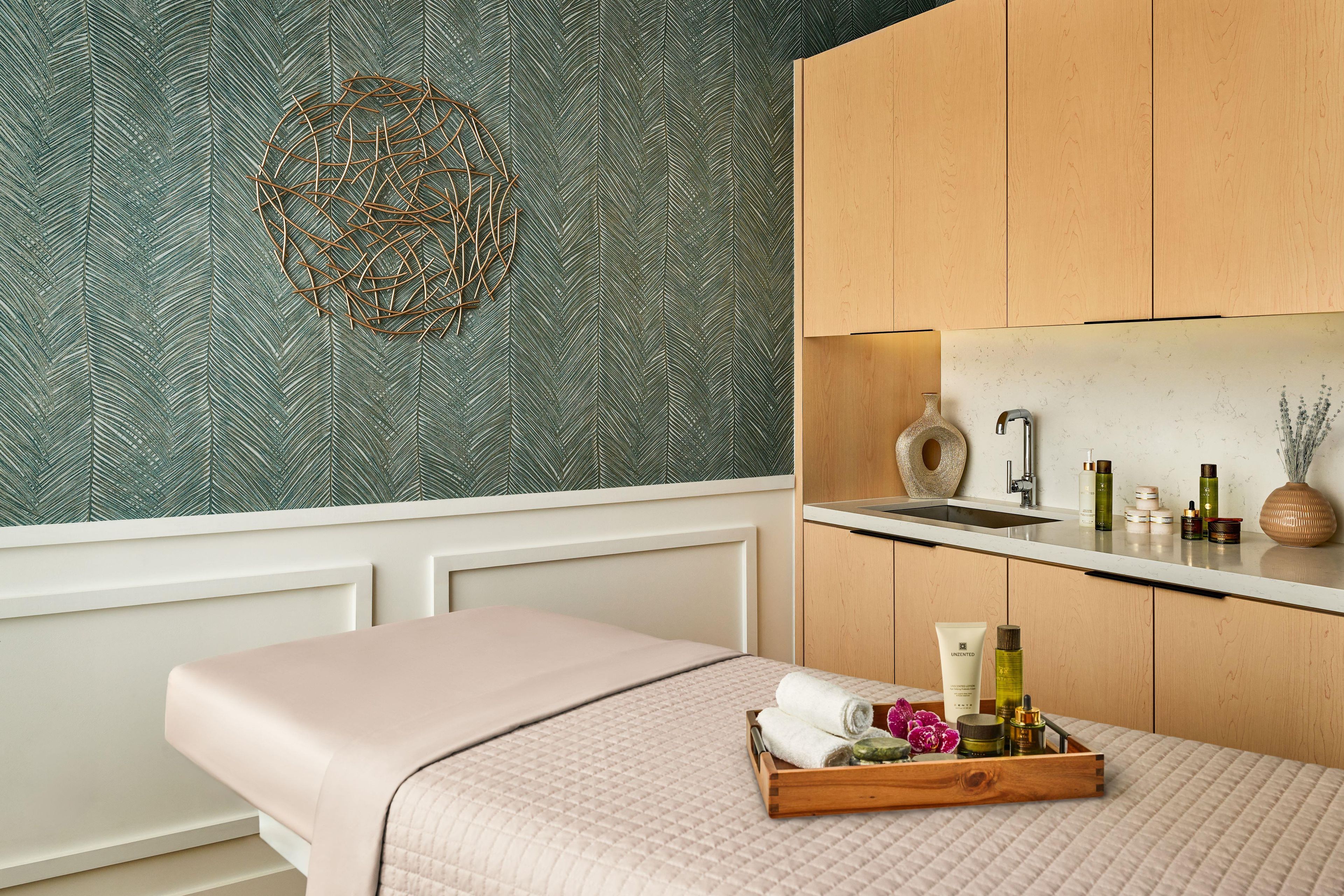 A spa room with a patterned wallpaper, a wooden cabinet, a sink, and a tray with toiletries.
